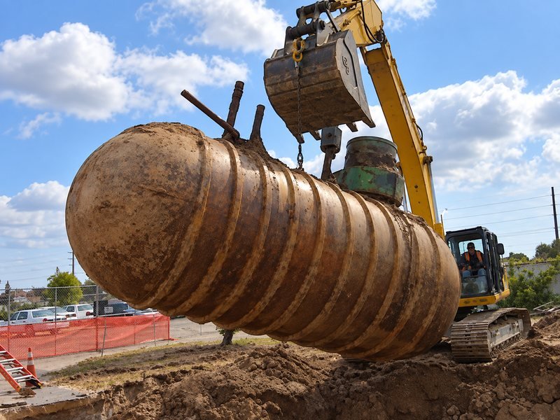 Excavator lifting a rusted underground tank