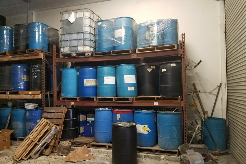 Drums and totes of hazardous waste stored on racks inside a warehouse